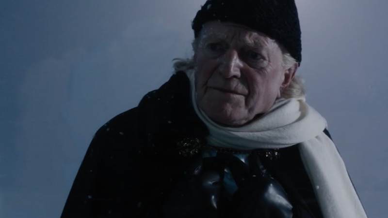 Image of David Bradley as The First Doctor wearing a hat and scarf in a snowy setting